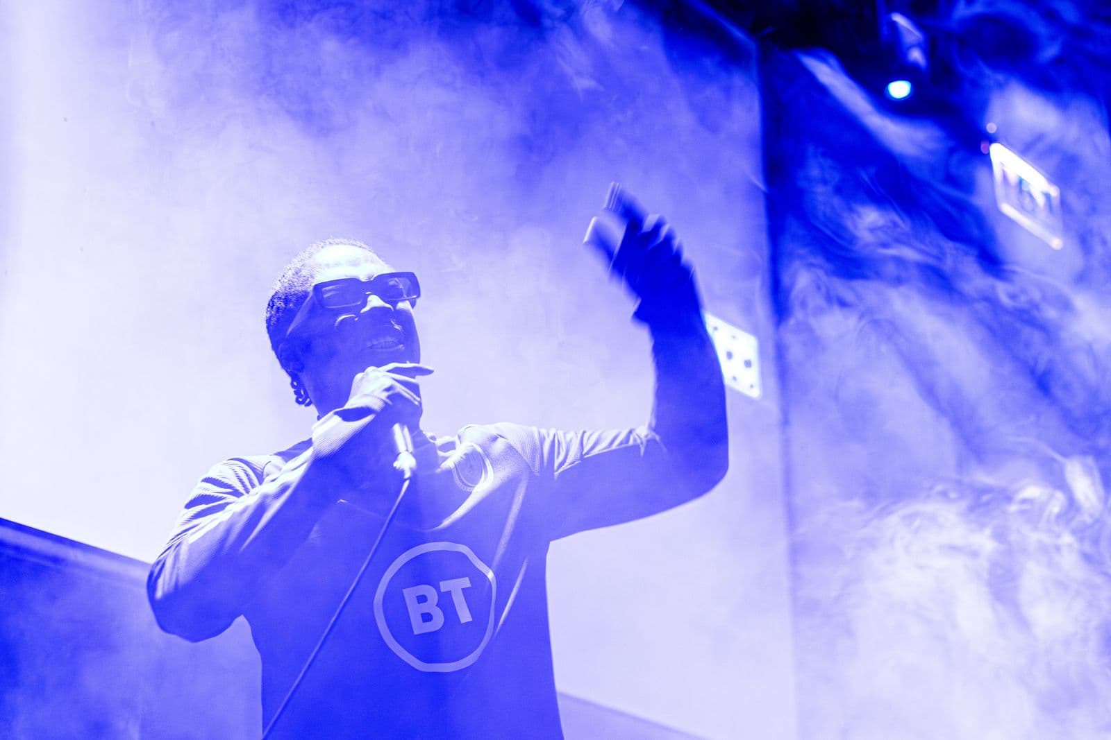 A performer on stage under blue light with one hand raised to the crowd